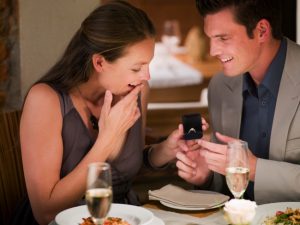Man surprising woman with engagement ring at restaurant table