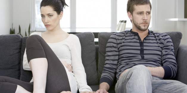 Couple sitting on sofa looking angry, touching hands